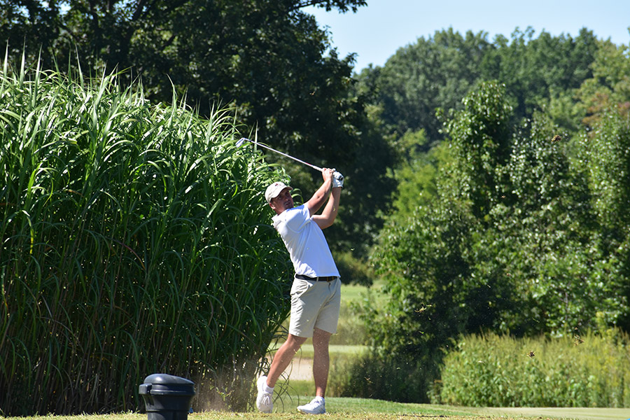 A male golfer takes a swing.